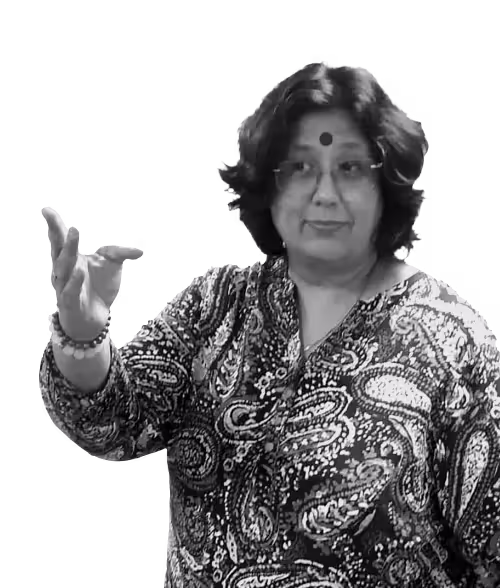 Woman with glasses and a bindi, wearing a patterned blouse, gesturing with her right hand.